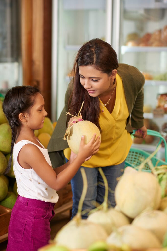 Little Indian girl giving her mother a melon in grocery store